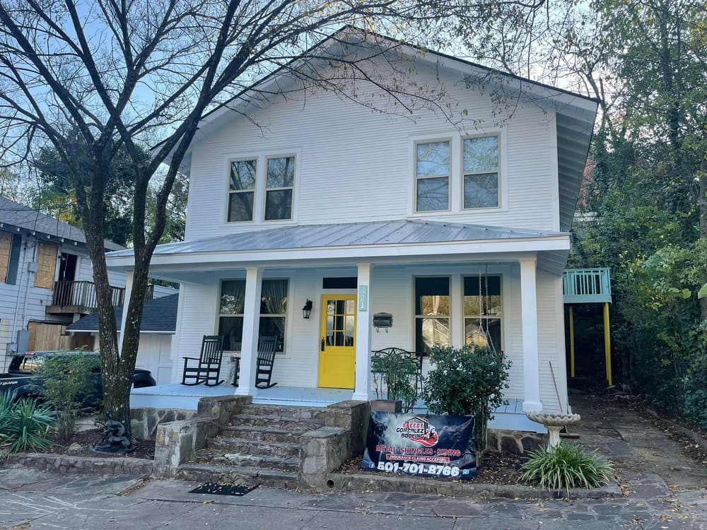 The same Hot Springs home after an exterior remodel, with fresh white siding, a new gray metal porch roof, white columns, and a yellow front door