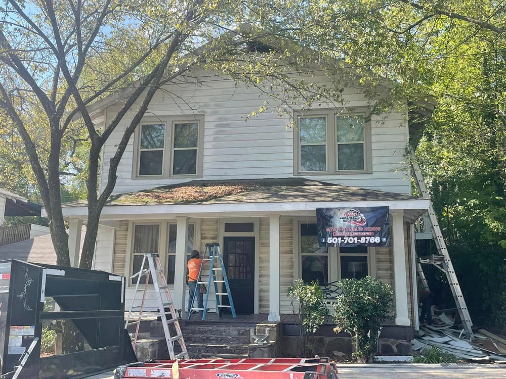A weathered white two-story Hot Springs home mid-remodel, with a worn porch roof and a Speedy Gonzalez crew on ladders