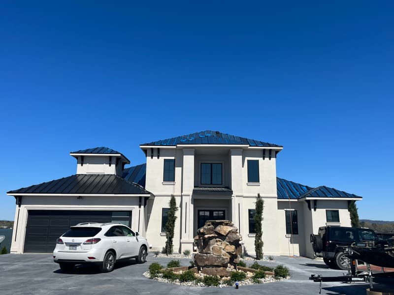 Dark standing seam metal roof on a large two-story lakefront home in the Hot Springs area, installed by Speedy Gonzalez Roofing