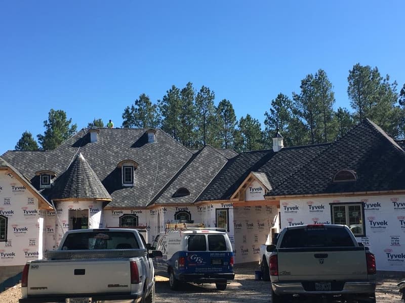 Large Hot Springs home mid-reroof, wrapped in house wrap with a roofer working near the ridge