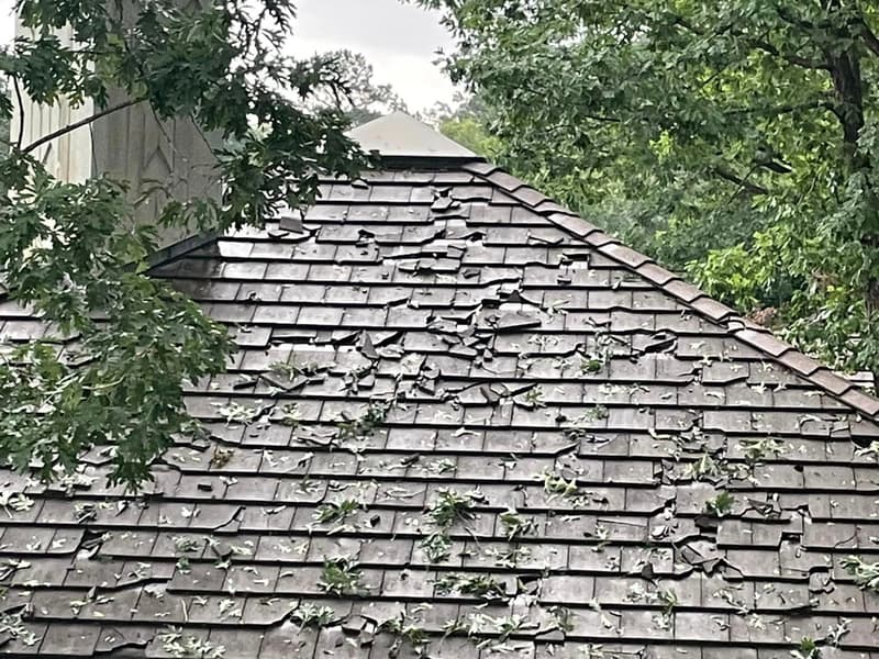 Cracked and lifted wood shake roof covered in fresh green leaf debris after a severe Arkansas storm